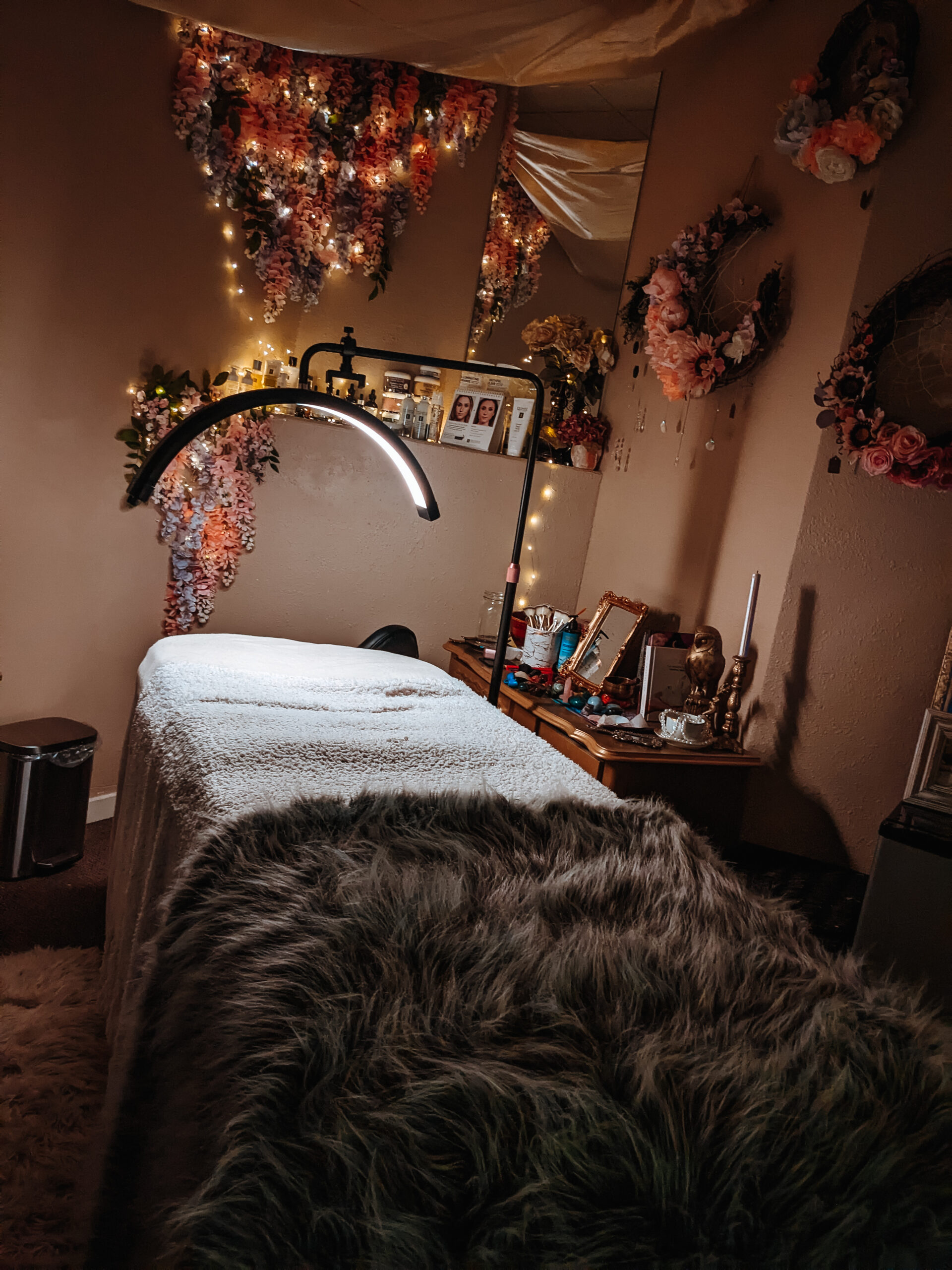 A magical image with fairy twinkle lights and hanging wisteria of a luxury esthetics spa room and a half moon spa lamp