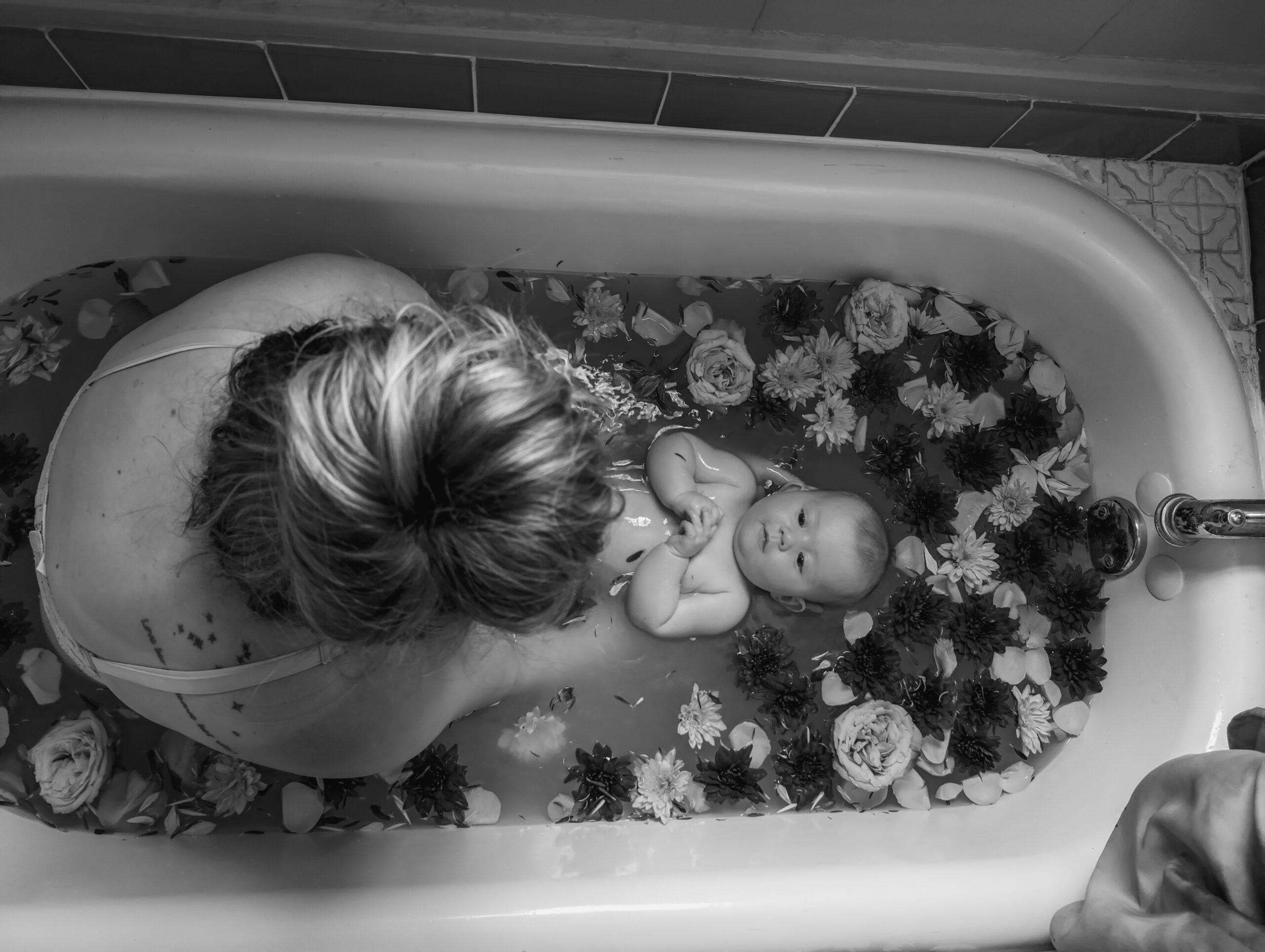 Mother and baby in a decorative floral bath in black and white for a Rebirthing Ritual.