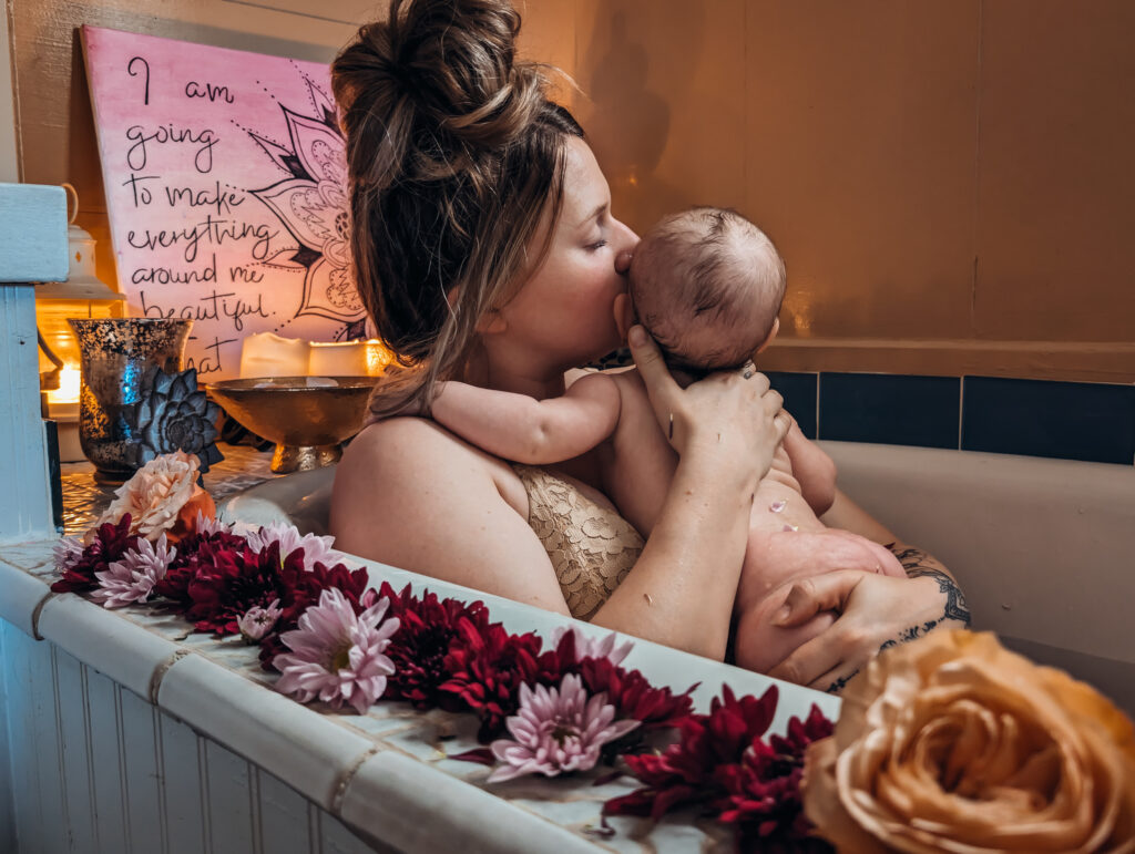 Mother holding baby in a floral bath for a Rebirthing Ritual